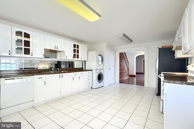 kitchen with white cabinetry, sink, range hood, stacked washer / dryer, and white appliances