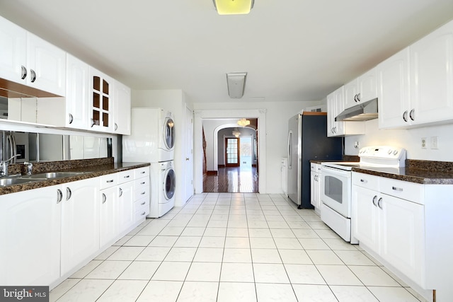 kitchen with white cabinetry, electric range, sink, stacked washer / dryer, and dark stone countertops