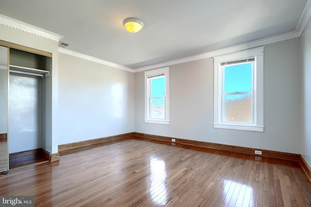 unfurnished bedroom with multiple windows, a closet, wood-type flooring, and ornamental molding