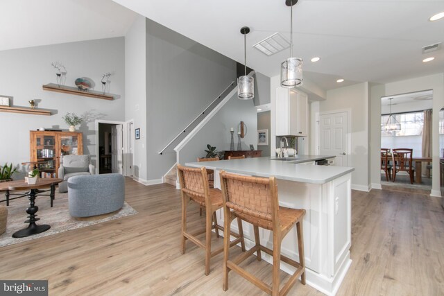 kitchen with white cabinets, light wood-type flooring, decorative light fixtures, kitchen peninsula, and a breakfast bar area