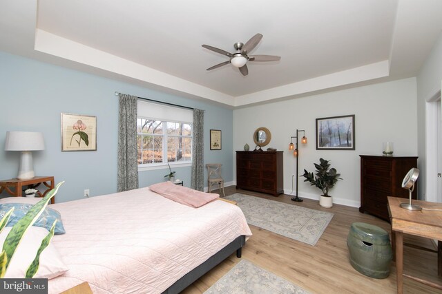 bedroom with a tray ceiling, ceiling fan, and light wood-type flooring