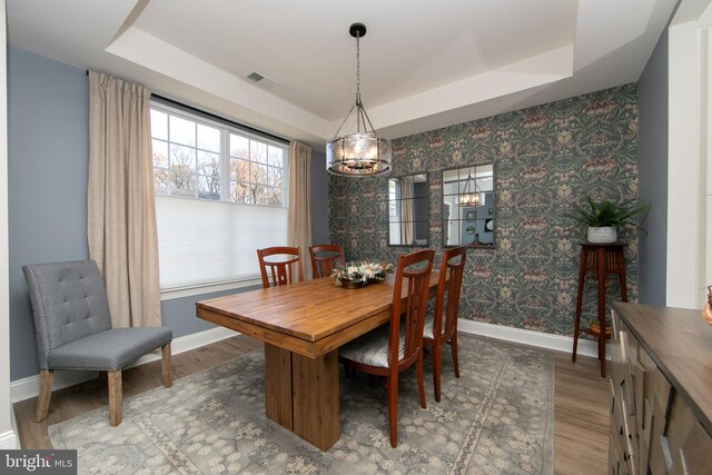 dining room with hardwood / wood-style floors, a raised ceiling, and an inviting chandelier