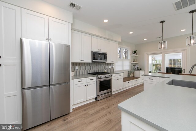 kitchen featuring sink, hanging light fixtures, light hardwood / wood-style flooring, white cabinetry, and stainless steel appliances