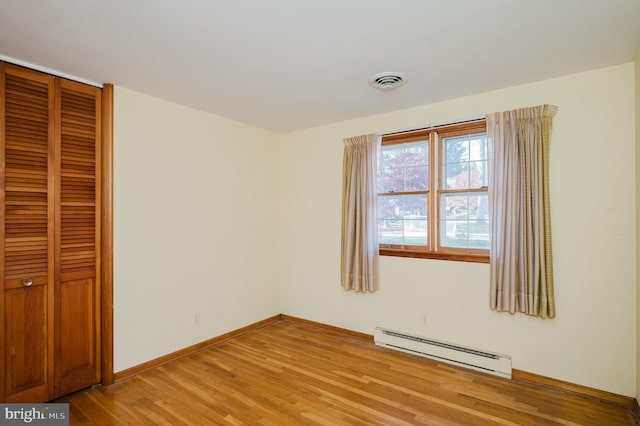 unfurnished bedroom featuring a closet, light hardwood / wood-style floors, and a baseboard heating unit