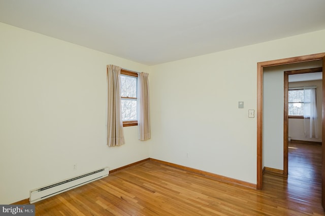 empty room with a wealth of natural light, baseboard heating, and wood-type flooring