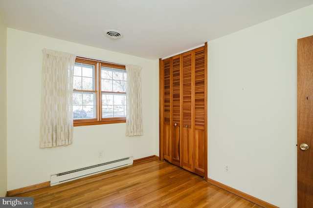 unfurnished bedroom featuring a closet, light wood-type flooring, and a baseboard heating unit