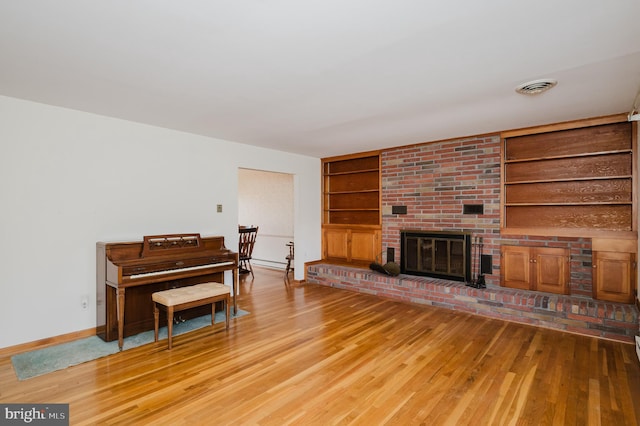 living room featuring a brick fireplace, light hardwood / wood-style flooring, and built in features