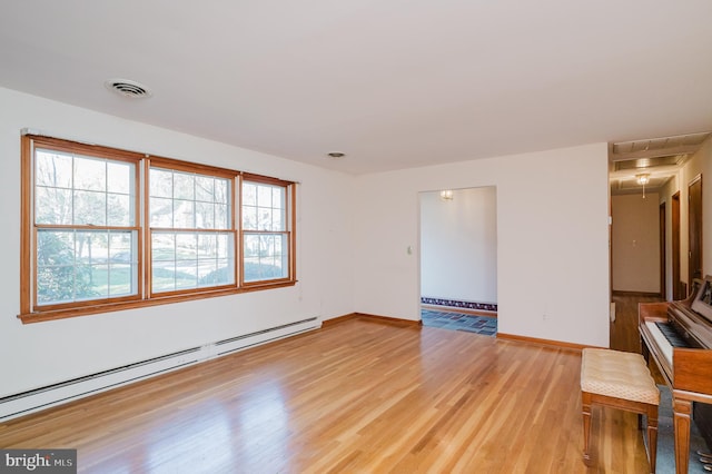 spare room featuring baseboard heating and light hardwood / wood-style floors