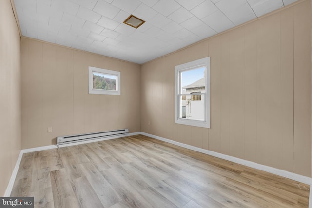 empty room featuring wood walls, light hardwood / wood-style floors, and a baseboard radiator