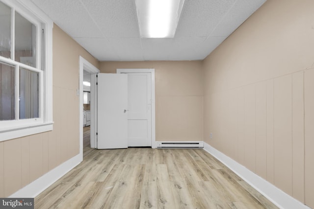 spare room featuring a baseboard radiator, light hardwood / wood-style flooring, and wood walls