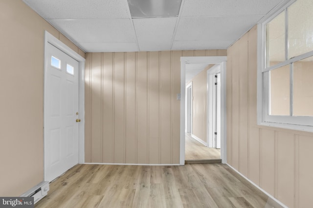 foyer entrance featuring a paneled ceiling, wood walls, plenty of natural light, and light hardwood / wood-style floors