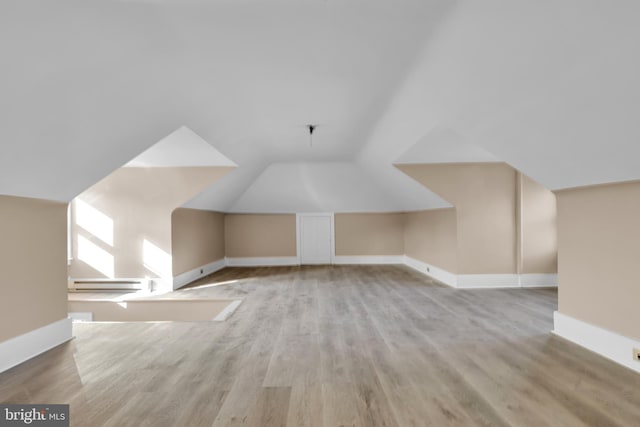 additional living space featuring light hardwood / wood-style flooring, a baseboard radiator, and vaulted ceiling