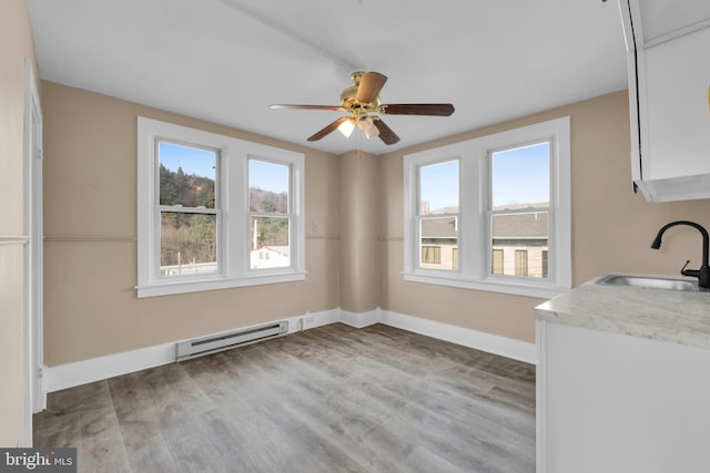 unfurnished dining area featuring baseboard heating, ceiling fan, sink, and wood-type flooring