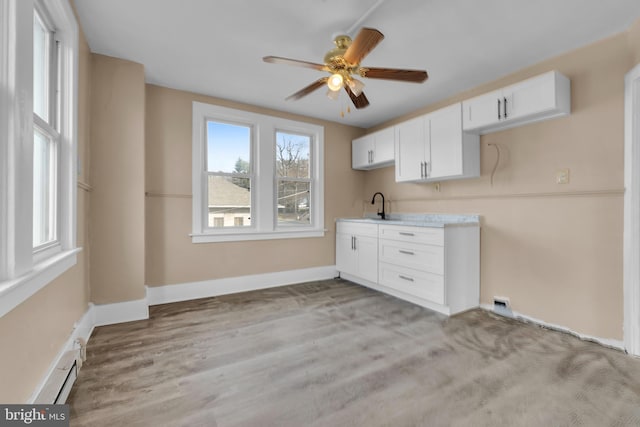 kitchen featuring light wood-type flooring, ceiling fan, a baseboard heating unit, sink, and white cabinetry