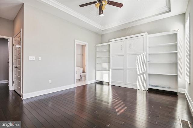 unfurnished bedroom featuring crown molding, connected bathroom, dark hardwood / wood-style flooring, a tray ceiling, and ceiling fan