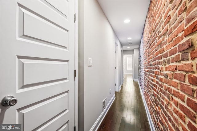 hallway with brick wall and dark hardwood / wood-style flooring