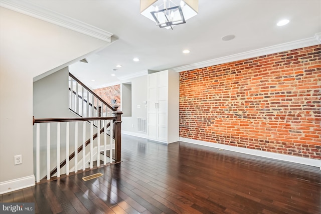 spare room with dark wood-type flooring, crown molding, and brick wall