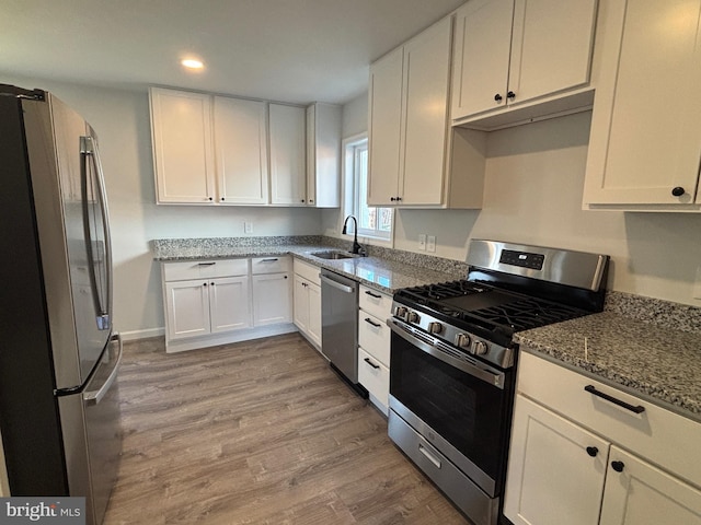 kitchen with light stone counters, stainless steel appliances, white cabinetry, sink, and light hardwood / wood-style flooring