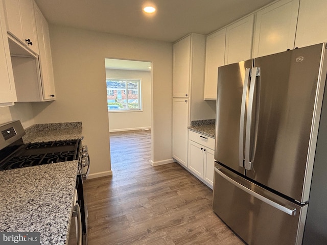 kitchen featuring light stone countertops, appliances with stainless steel finishes, light hardwood / wood-style floors, and white cabinets