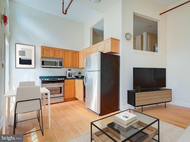 kitchen featuring high vaulted ceiling, stainless steel appliances, light brown cabinetry, and light hardwood / wood-style flooring