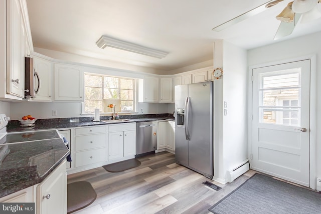 kitchen with light wood-type flooring, stainless steel appliances, ceiling fan, a baseboard heating unit, and white cabinetry