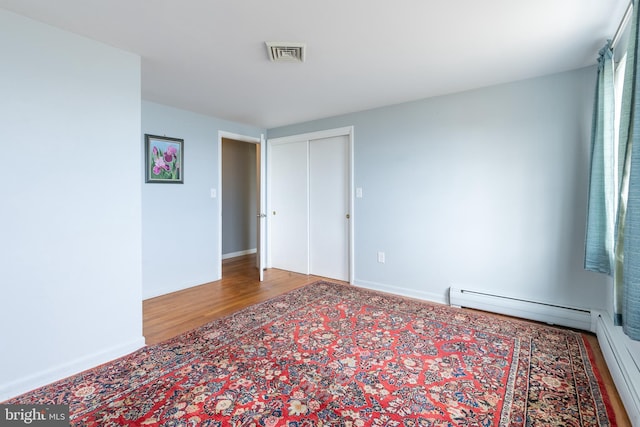 empty room with hardwood / wood-style flooring and a baseboard heating unit