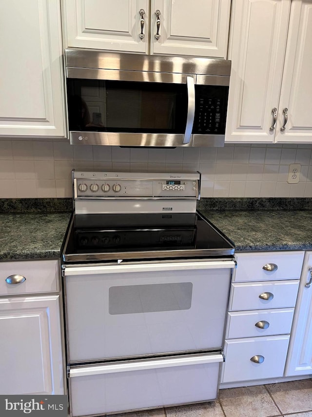 kitchen featuring white cabinetry, dark stone counters, white range oven, and tasteful backsplash