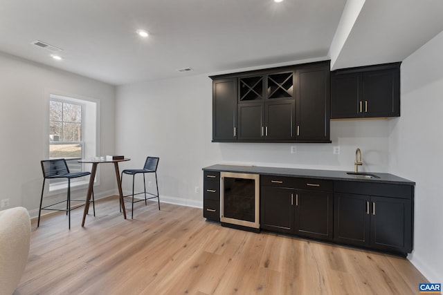 bar with light hardwood / wood-style floors, sink, and beverage cooler