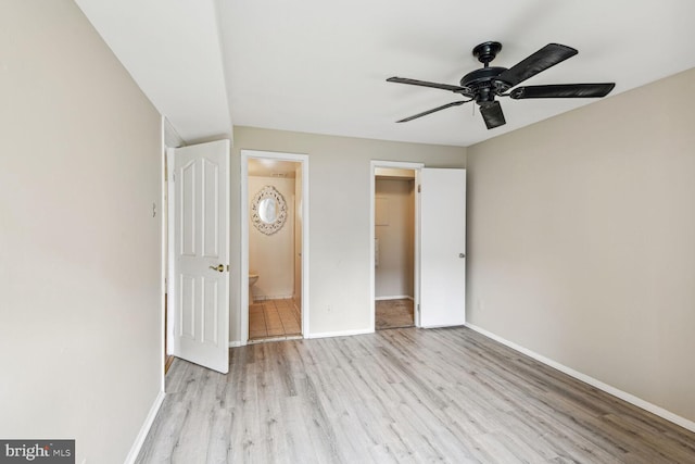 unfurnished bedroom featuring ensuite bath, a walk in closet, ceiling fan, and light wood-type flooring