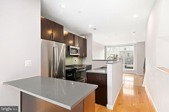 kitchen featuring appliances with stainless steel finishes, light hardwood / wood-style floors, an island with sink, decorative backsplash, and sink