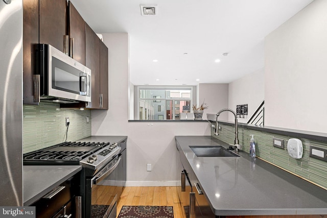 kitchen featuring stainless steel appliances, sink, light wood-type flooring, decorative backsplash, and dark brown cabinetry