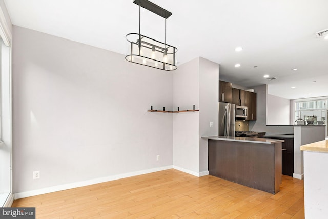 kitchen with stainless steel appliances, light wood-type flooring, tasteful backsplash, kitchen peninsula, and dark brown cabinetry