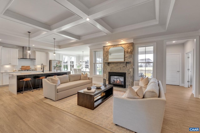 living room featuring beam ceiling, an inviting chandelier, a fireplace, coffered ceiling, and light wood-type flooring