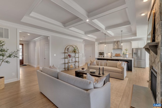 living room featuring crown molding, a stone fireplace, light wood-type flooring, beam ceiling, and coffered ceiling