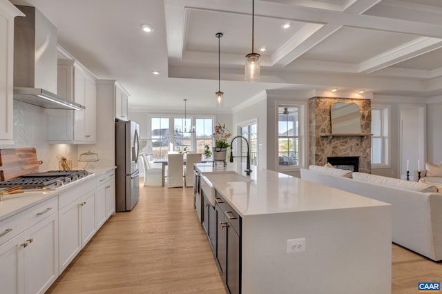 kitchen featuring a center island with sink, white cabinets, wall chimney exhaust hood, pendant lighting, and light wood-type flooring