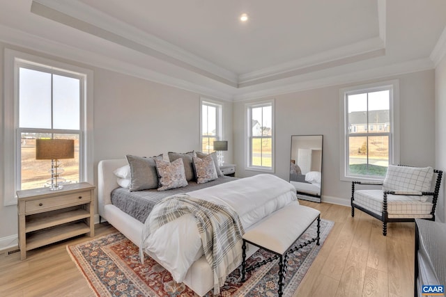 bedroom featuring light hardwood / wood-style floors, multiple windows, a raised ceiling, and crown molding