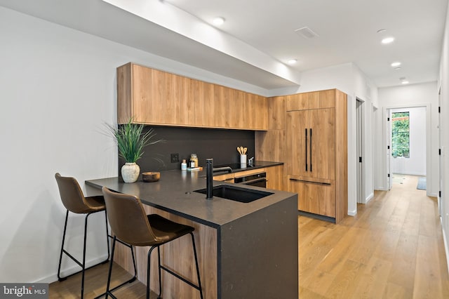 kitchen with paneled fridge, sink, light hardwood / wood-style floors, a breakfast bar, and kitchen peninsula