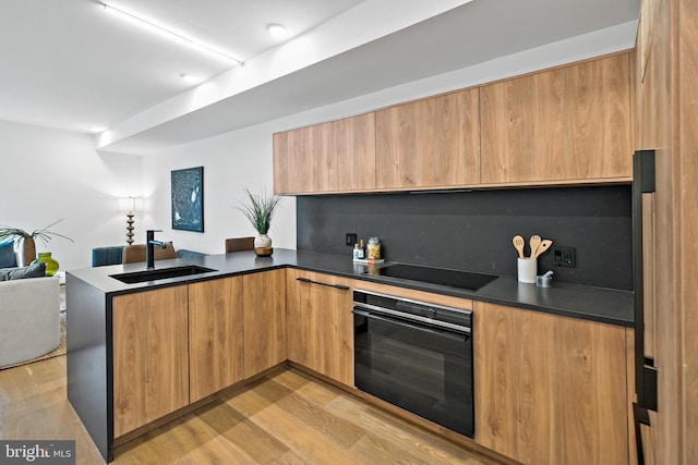 kitchen with kitchen peninsula, black appliances, sink, and light wood-type flooring