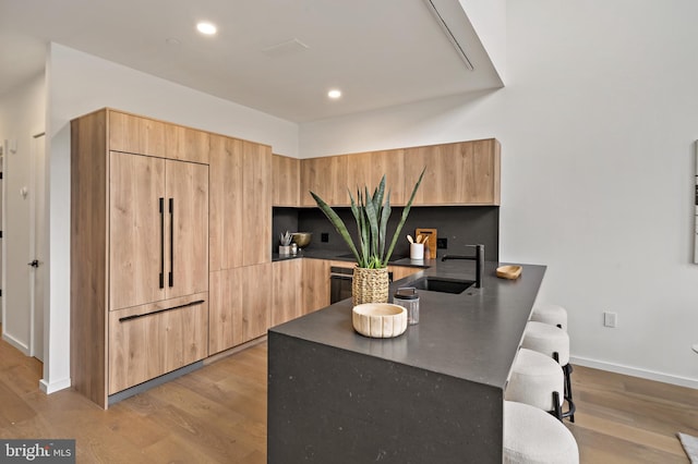 kitchen with light brown cabinetry, sink, light hardwood / wood-style floors, and paneled built in fridge