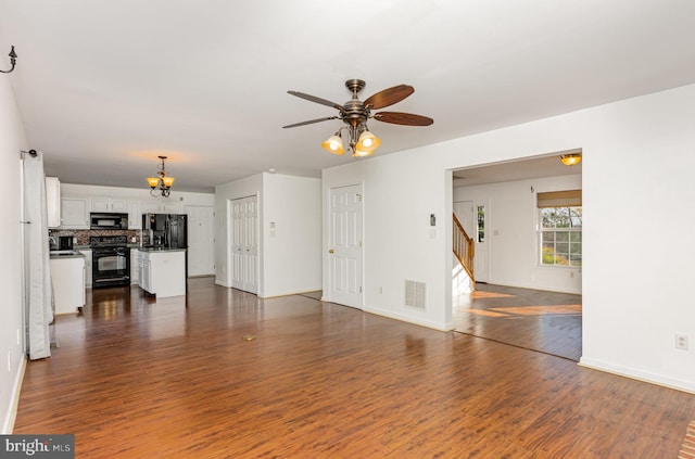 unfurnished living room featuring ceiling fan with notable chandelier and dark hardwood / wood-style floors