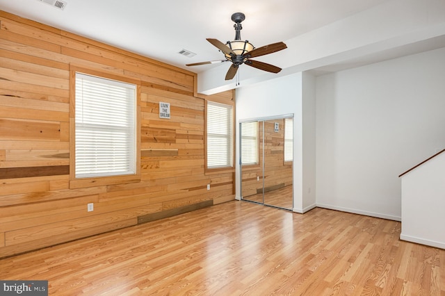 unfurnished room with light hardwood / wood-style floors, ceiling fan, a healthy amount of sunlight, and wood walls