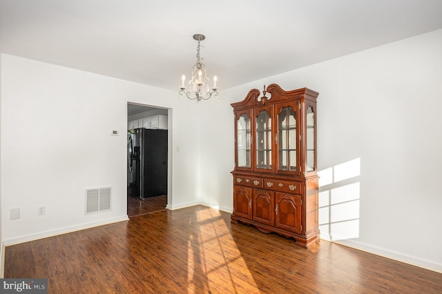 unfurnished dining area featuring an inviting chandelier and dark wood-type flooring