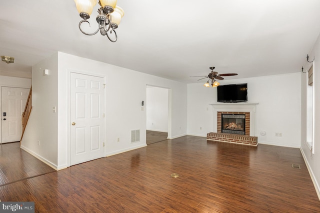 unfurnished living room with ceiling fan with notable chandelier, dark hardwood / wood-style floors, and a brick fireplace