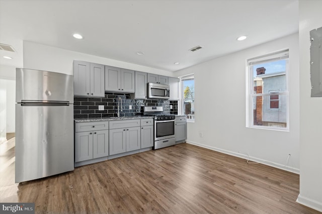 kitchen featuring gray cabinetry, light stone countertops, stainless steel appliances, light hardwood / wood-style flooring, and decorative backsplash