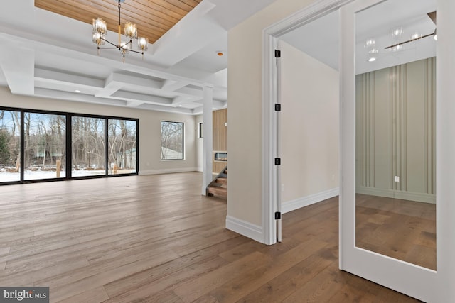 empty room featuring coffered ceiling, beamed ceiling, wood-type flooring, and a notable chandelier