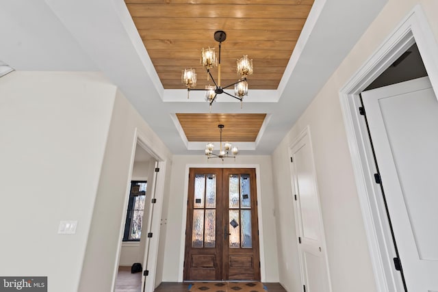 foyer entrance with french doors, wood ceiling, a tray ceiling, and a chandelier