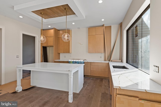 kitchen with light stone countertops, a kitchen island, decorative light fixtures, dark wood-type flooring, and a tray ceiling