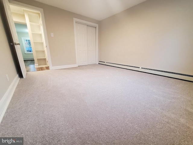 unfurnished bedroom with light carpet, a closet, and a baseboard heating unit