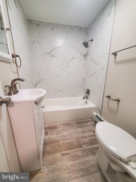 full bathroom featuring tiled shower / bath combo, toilet, vanity, and a baseboard heating unit