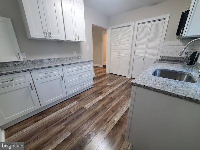 kitchen featuring white cabinetry, sink, light stone countertops, tasteful backsplash, and dark hardwood / wood-style flooring